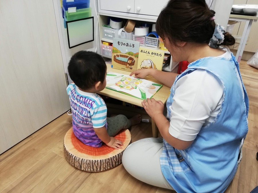 プチリック美野里園の写真19枚目：保育者と一緒に絵本を読んでいます